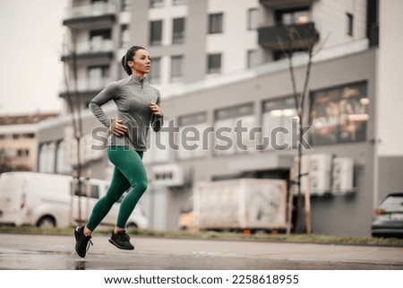 An urban female runner is running on the rainy day on city street. Royalty-Free Stock Photo #2258618955