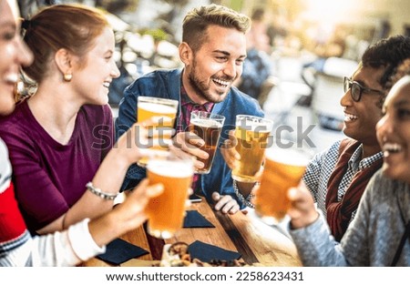 Young people drinking beer pints at brewery bar garden - Genuine beverage life style concept with guys and girls sharing happy hour together at open air pub dehor - Warm sunset backlight filter Royalty-Free Stock Photo #2258623431