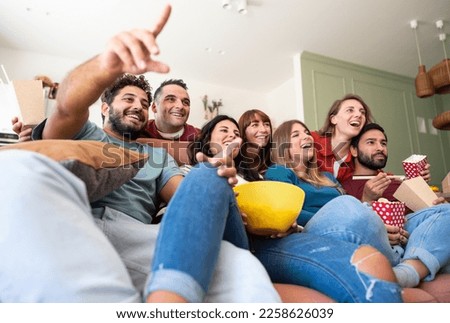 A group of Caucasian friends sitting on the couch and watching TV while eating popcorn, chips, and Chinese food. They enjoy each other's company and having fun together. Royalty-Free Stock Photo #2258626039