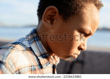 Outdoor profile view image of angry african american frustrated offended boy kid walking quickly in city street after quarrel with his mom or friends. Children, their emotions and facial expressions Royalty-Free Stock Photo #2258633881