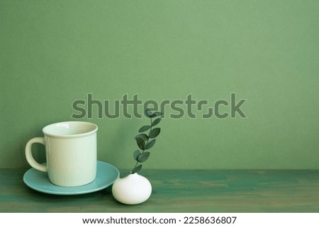 Coffee cup and eucalyptus leaf on wooden table. green wall background. minimal, copy space