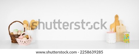 Easter theme kitchenware, utensils and decor on a white shelf or counter. Banner against a white wall background with copy space. Spring home kitchen cooking concept. Royalty-Free Stock Photo #2258639285
