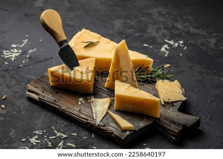 Parmesan cheese on a wooden board, Hard cheese, rosemary and cheese knife on a dark background. place for text, top view. Royalty-Free Stock Photo #2258640197