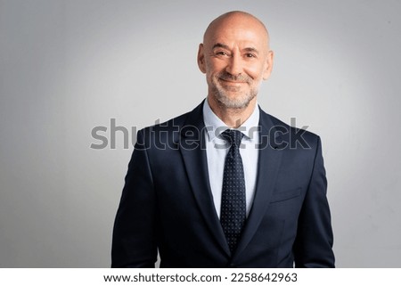 Portrait of caucasian business man looking at camera and smiling. Confident mature male professional is in suit. He is against gray background. Royalty-Free Stock Photo #2258642963