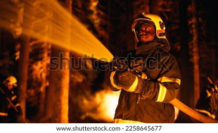 Calm and Collected African American Firefighter Extinguishing a Wildland Fire Deep in a Forest. Professional in Safety Uniform and Helmet Using a Fire Hose to Battle Dangerous Wildfire. Royalty-Free Stock Photo #2258645677