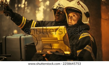 Professional Firefighters Extinguishing Forest Fire: Female Squad Leader Talking with African American Fireman, Using Laptop Computer Near Wildfire, Discussing the Situation. Close Up Shot. Royalty-Free Stock Photo #2258645753