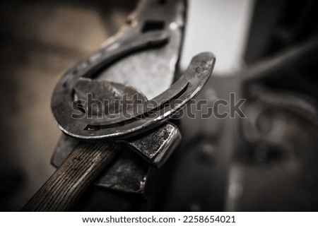 Closeup of Metal Horseshoe Laying on the Blacksmith Hammer. Horse Farrier Work Equipment. Equestrian Theme. Royalty-Free Stock Photo #2258654021