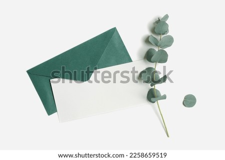 Teal envelope and empty paper card mock up with green plant eucalyptus on white background. White blank open letter on table. Minimal design stationery, flat lay template, top view, copy space. 