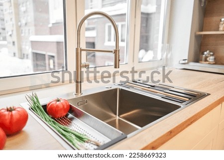 Stylish metallic crane at the kitchen. Sink faucet at the kitchen. Metal crane in close-up photo. Details of the interior of the kitchen in the house. Royalty-Free Stock Photo #2258669323
