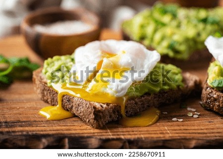 Breakfast Rye Bread Toast With Mushed Avocado And Poached Egg On Wooden Serving Board, Closeup View Royalty-Free Stock Photo #2258670911