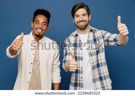 Young two friends satisfied smiling happy men 20s wear white casual shirts look camera together showing thumb up like gesture isolated plain dark royal navy blue background. People lifestyle concept