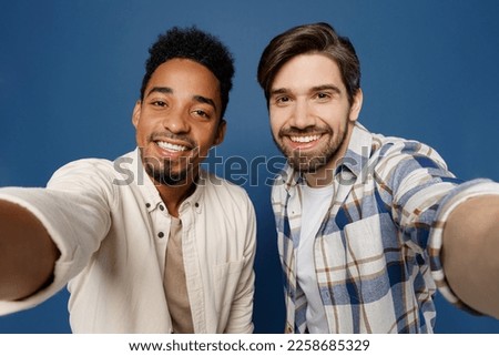 Close up young two friends men 20s wear white casual shirts together looking camera doing selfie shot pov on mobile cell phone isolated plain dark royal navy blue background. People lifestyle concept