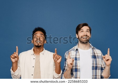Young two friends men wear white casual shirts together point index finger overhead indicate on workspace copy space mock up isolated plain dark royal navy blue background. People lifestyle concept Royalty-Free Stock Photo #2258685333