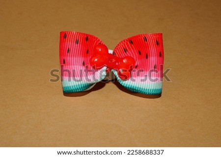 a red and green bow in the color of a watermelon with a red bone in the middle lies on a beige background.  accessories for dogs with long hair