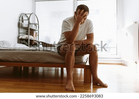 concept of life-weary, suffering, sick man. middle-aged man suffering from insomnia, depression, sits on bed with head down and covers face with hands. Royalty-Free Stock Photo #2258693083