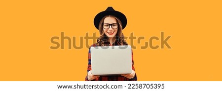Portrait of modern happy smiling young woman working with laptop wearing eyeglasses on orange background, blank copy space for advertising text