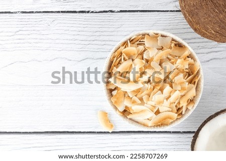 Coconut chips or coconut flakes on a white wooden background. Healthy snacks. Coconut dessert. Top view. Copy space. Royalty-Free Stock Photo #2258707269