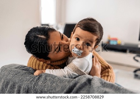 Stock photo of young mother kissing her little baby in the sofa.