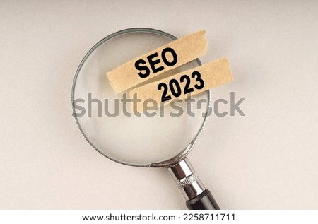 On the magnifying glass are paper strips with the inscription - SEO 2023.