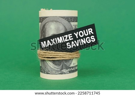Business concept. On a green surface, rolled dollars with a black sign that says - Maximize your savings Royalty-Free Stock Photo #2258711745