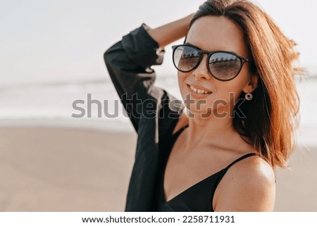 Close up portrait of smiling excited stylish woman with short dark hairstyle posing to camera with happy emotions on blur background of ocean 