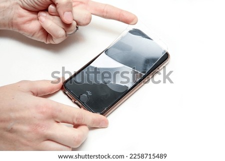 The detail of the hands removing the broken protection glass with cracks from the smartphone touch screen. 
