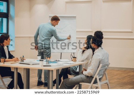 Multiracial professional project managers group negotiating in boardroom at meeting. Rear view of a redhead businessman writing on a flipchart board during a staff meeting. Copy space.