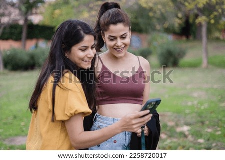 Smiling girls in the park, one of them showing pictures on her cell phone.