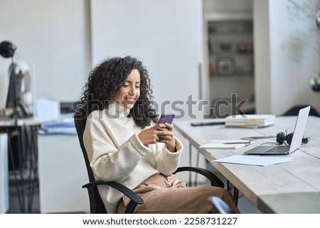 Young happy hispanic business woman office worker looking at smartphone using mobile cell phone technology, professional businesswoman executive working in office typing on cellphone sitting at desk. Royalty-Free Stock Photo #2258731227