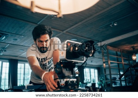 Director of photography with a camera in his hands on the set. Professional videographer at work on filming a movie, commercial or TV series. Filming process indoors, studio Royalty-Free Stock Photo #2258734261