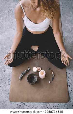 High angle of female yogi practicing mindfulness in lotus pose on yoga mat while doing energy clearing ritual with herbal wrap and candles Royalty-Free Stock Photo #2258736565