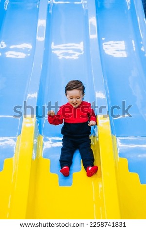 Happy, smiling little boy, preschool child descends, slides down a plastic slide on an indoor playground. Photography, childhood and emotions concept.