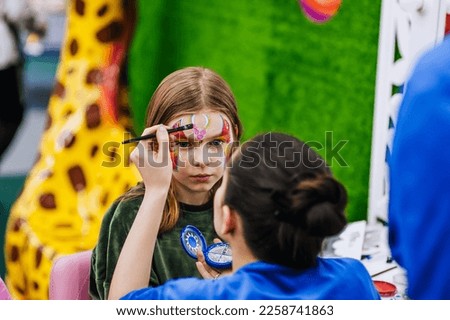 A professional make-up artist, woman artist draws, makes face painting, children's make-up with paints for a little girl, a child. Photography, art, creativity concept, lifestyle. Royalty-Free Stock Photo #2258741863