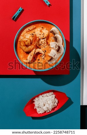 Tom yum soup with shrimps and rice in blue pastel color boul at blue and red background with sunlight and shadows, minimalism,top view. Royalty-Free Stock Photo #2258748711