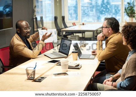 Confident African American broker presenting graphic financial data to his colleagues during discussion of marketing development