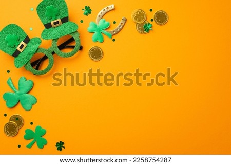 Saint Patrick's Day concept. Top view photo of green hat shaped party glasses gold coins horseshoe clovers and trefoil shaped confetti on isolated orange background with copyspace