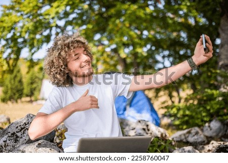 A mountaineer taking a photo while resting in a natural forest next to a tent