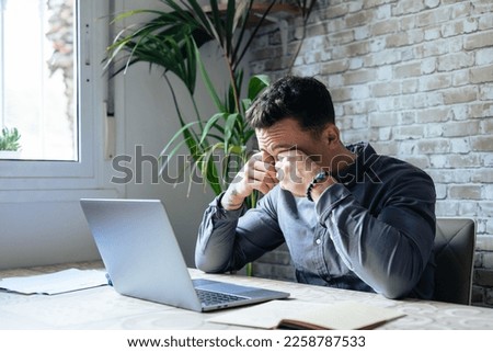 Tired young man feel pain eyestrain holding glasses rubbing dry irritated eyes fatigued from computer work, stressed man suffer from headache bad vision sight problem sit at home table using laptop Royalty-Free Stock Photo #2258787533