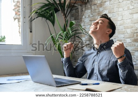 Man sit at desk read e-mail on laptop makes yes gesture feels happy. Male entrepreneur get great business news, celebrate career growth, advance. Achievement, win, moment of auction victory concept Royalty-Free Stock Photo #2258788521