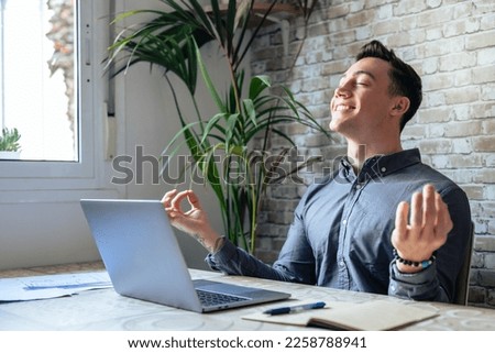 Serene office male employee sit at desk relaxing doing yoga, practice meditation to reduce stress relief fatigue feel internal balance at workplace, improve mindfulness, maintain mental health concept Royalty-Free Stock Photo #2258788941