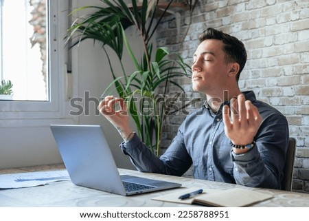 Serene office male employee sit at desk relaxing doing yoga, practice meditation to reduce stress relief fatigue feel internal balance at workplace, improve mindfulness, maintain mental health concept Royalty-Free Stock Photo #2258788951
