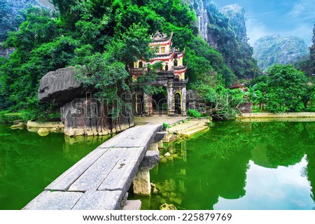 Outdoor park landscape with lake and stone bridge. Gate entrance to ancient Bich Dong pagoda complex. Ninh Binh, Vietnam travel destination Royalty-Free Stock Photo #225879769