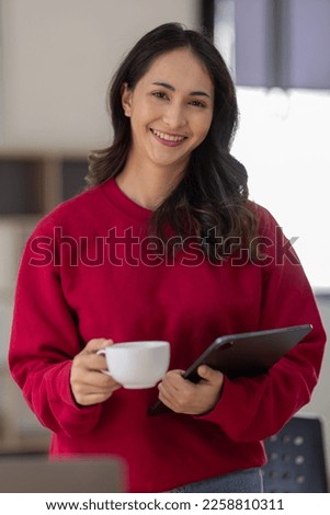 Image of young indian girl asian woman, company worker in dress red shirt, smiling and holding digital tablet, standing over office background