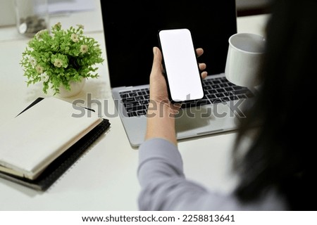 Close-up, back view image, An Asian female office worker using her smartphone at her desk, phone white screen mockup.