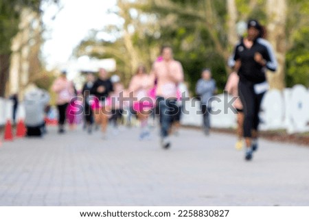 Defocused photo of women running a 5k road race as part of a breast cancer charity benefit