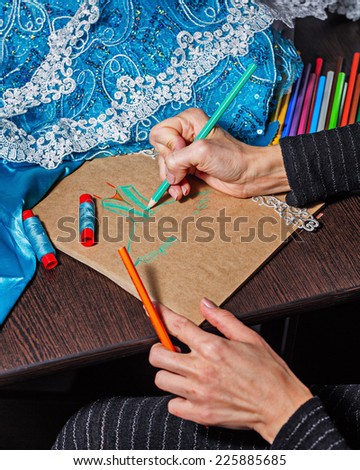 Fashion designer draws a sketch of the future dress on paper, beside lie thread and lace
