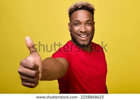 Photograph of an excited, rejoicing, overjoyed man, delighted that he got isolated on a yellow background. Black man shows Like sign