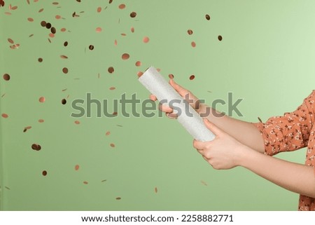 Young woman blowing up party popper on green background, closeup
