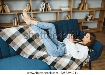 Young beautiful woman wearing white t-shirt on textile sofa at home. Attractive slim female in domestic situation, resting on couch in her lofty apartment. Background, copy space, close up