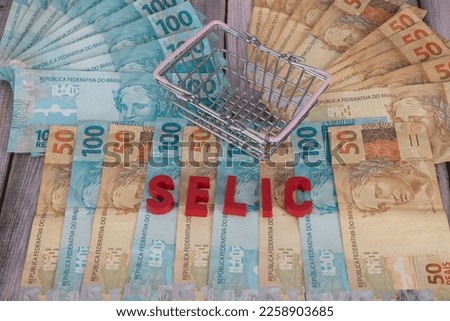Notes of 50 and 100 reais on wood with a mini supermarket basket, with the word SELIC which means in Portuguese "Special System of Liquidation and Custody" in English, 
